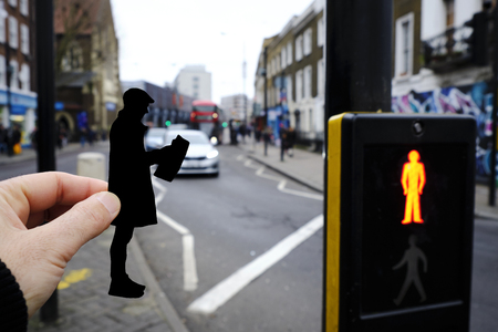 closeup of the hand of a man holding a paper cutout in the shape of a man, wearing a flat cap and a coat, reading the newspaper on the street, in London, United Kingdomの写真素材