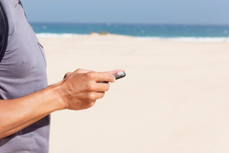 closeup of a young caucasian man, wearing a T-shirt and carrying a backpack, using a smartphone on a...