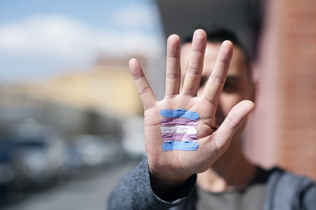 closeup of the palm of the hand of a young caucasian person with a transgender flag painted in it, in front of his or her faceの写真素材