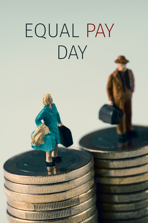 a miniature woman and a miniature man on the top of two equal piles of euro coins and the text equal pay dayの写真素材
