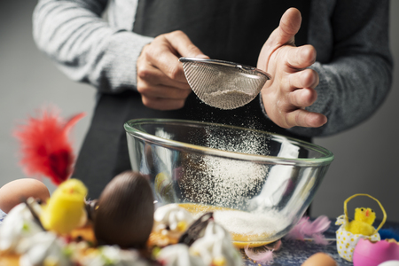 man preparing a typical mona de pascua, a cake eaten in Spain on Easter Monday, decorated with a chocolate egg, a teddy chick and feathers of different colorsの写真素材