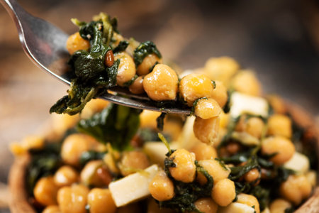 closeup of a chickpea salad, with cooked spinach, pine nuts, onion and cheese, served in a rustic...