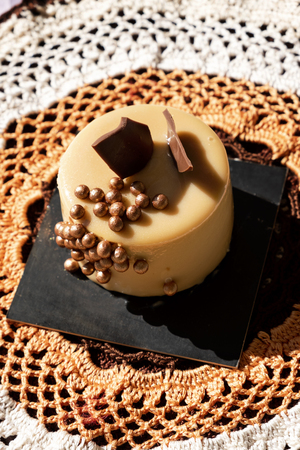 high angle view of an appetizing cake, ornamented with candy pearls and pieces of chocolate, on a square black surface placed on a beige and brown crocheted doilyの写真素材