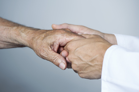 closeup of a caucasian man, in a white coat, moving the hand of a senior caucasian patient manの写真素材