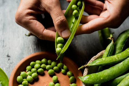 high angle view of a young caucasian man removing green peas from a pea pod with his fingers and...