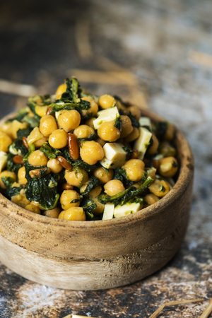 closeup of a chickpea salad, with cooked spinach, pine nuts, onion and cheese, served in a rustic boxwood bowl, placed on a rustic tableの写真素材