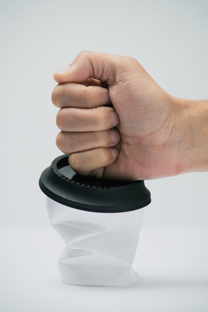 closeup of a man smashing a white plastic cup, covered with a black lid, on a white backgroundの写真素材