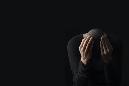 closeup of a desperate young caucasian man with his hands in his head, against a black background, with some blank space on the leftの写真素材