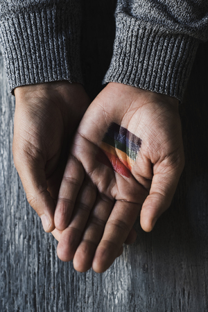 high angle view of the hands of a young caucasian person, with a rainbow flag in one of them, on a gray rustic wooden surfaceの写真素材