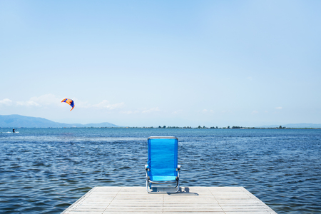 a lonely blue deck chair at the end of a wooden pier next to the water, with a blank space on the clear skyの写真素材