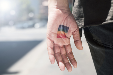 closeup of a rainbow flag in the palm of the hand of a young caucasian person, wearing casual clothing, seen from behind, on the streetの写真素材