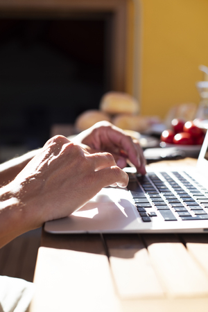 closeup of a young caucasian man using a laptop sitting at a wooden table outdoors during a mealの写真素材