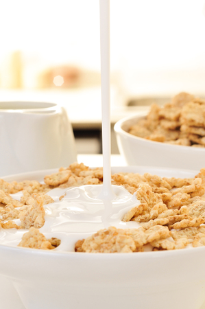 closeup of a bowl with breakfast cereals soaked in milk or drinkable yogurt, on a table set for breakfastの写真素材
