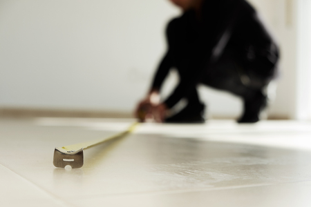 closeup of a young caucasian man using a measuring tape on a beige tiled floorの写真素材