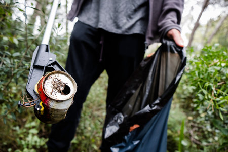 closeup of a caucasian man collecting garbage with a trash grabber stick, in a forest, as an action...