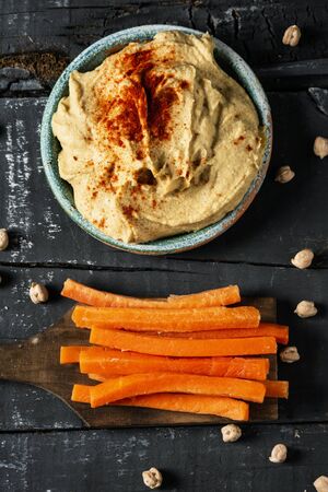 high angle view of a homemade hummus seasoned with paprika served in a green ceramic plate and some strips of carrot, to dip in it, on a dark gray rustic wooden tableの写真素材
