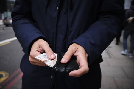 closeup of a young caucasian man on the street putting in or taking off some pound sterling banknotes from his walletの写真素材