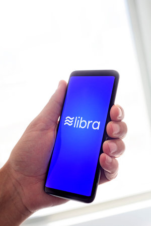 BARCELONA, SPAIN - JUNE 20, 2019: A young caucasian man uses a smartphone, with the logo of Libra,...