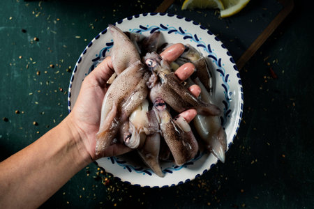 high angle view of a man with some raw squids in his hand, on a dark green table