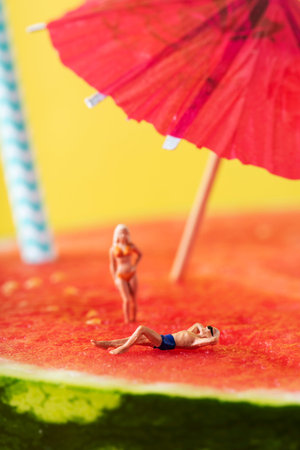 a miniature man and a miniature woman wearing swimsuit relaxing on a refreshing ripe watermelon,...