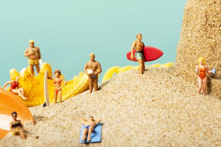 some different miniature people wearing swimsuit carrying surfboards or relaxing on the sand of the beach next to a seashellsの写真素材