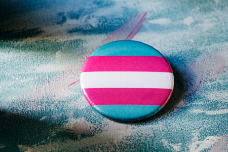 closeup of a badge patterned with a transgender pride flag on a surface painted with brushstrokes of...