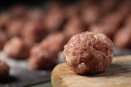 closeup of a raw meatball on a wooden chopping board placed on a table and some other meatballs in the backgroundの写真素材