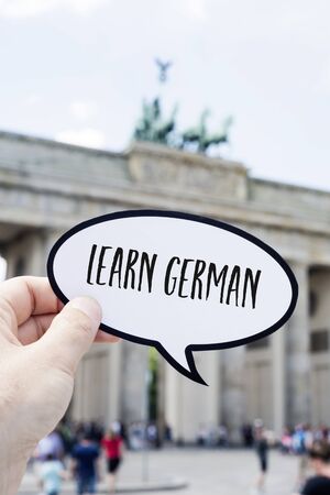 closeup of the hand of a young man showing a speech bubble with the text learn German written in it, in front of the Brandenburg Gate in Berlin, Germanyの写真素材