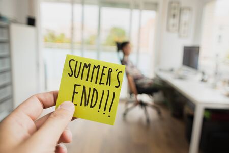 closeup of a man with a note in his hand, with the text summers end written in it, and a man sitting at his office desk in the backgroundの写真素材