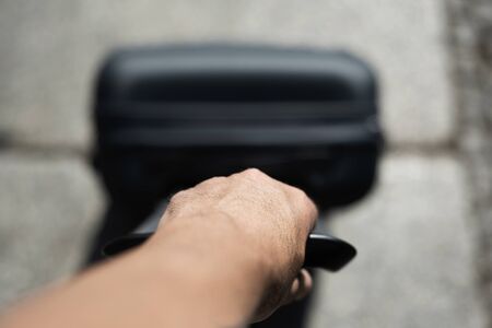closeup of a young caucasian man, seen from above, pulling a trolley by its handle on the streetの写真素材