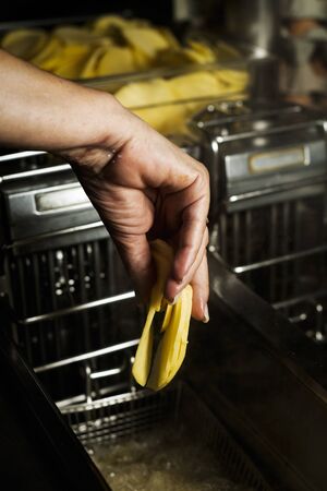 closeup of a woman in a professional kitchen about to fry some sliced potatoes in a deep fryerの写真素材