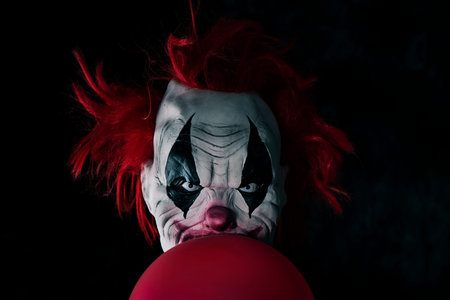 closeup of a scary evil clown with red hair and white eyes, staring at the observer, with a red...