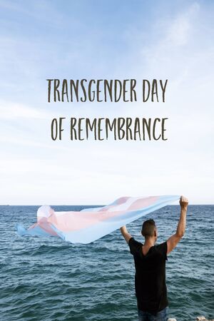 Young caucasian person in front of the sea holding a transgender pride flagの写真素材