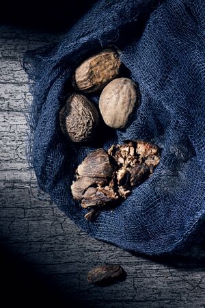 Closeup of some shelled and dried nutmeg seeds in a dark gray gauze fabric, on a gray wooden table slightly illuminatedの写真素材