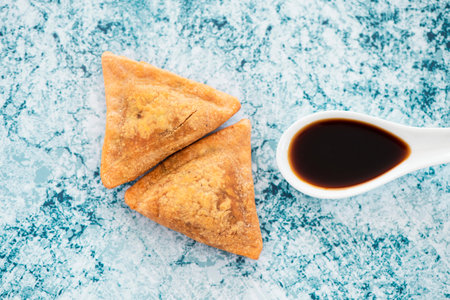 High angle view of some Indian samosas and a ceramic spoon with a dark sauce on a marbled stone...