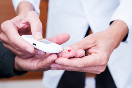 Closeup of a young caucasian medic man  measure the blood glucose level of an old caucasian man in a...