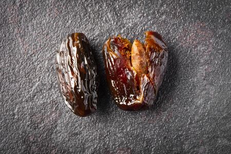 Two ripe date fruits, one of them whole and the other one smashed, on a dark gray stone surfaceの写真素材
