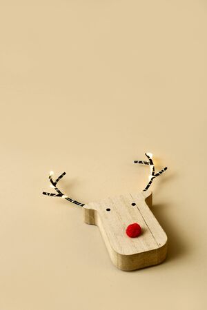 a funny wooden reindeer head, with a red nose, on a brown background with some blank space on topの写真素材