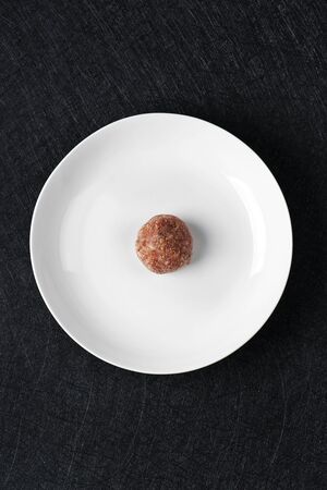 high angle view a raw homemade meatball in the center of a white ceramic plate, on a black stone table or countertopの写真素材