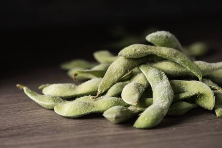Closeup of a pile of frozen edamame, Japanese green soybeans in the pod, on a wooden table or counter topの写真素材