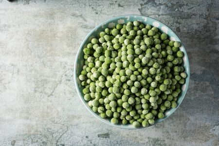 high angle view of a pile of frozen green peas in a light blue ceramic bowl, on a tableの写真素材