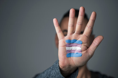 Closeup of the palm of the hand of a young caucasian person with a transgender flag painted in it, in front of his or her faceのeditorial素材