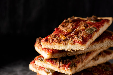 closeup of some pieces of coc de tomata, a savory flat pie made with tomato and tuna typical of...