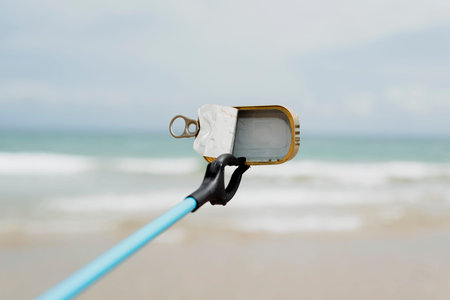 closeup of someone collecting garbage with a reach extender, in a lonely beach, as an action to...