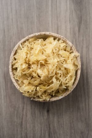 high angle view of an earthenware bowl with cooked sauerkraut, german finely cut fermented cabbage, on a wooden surfaceの写真素材