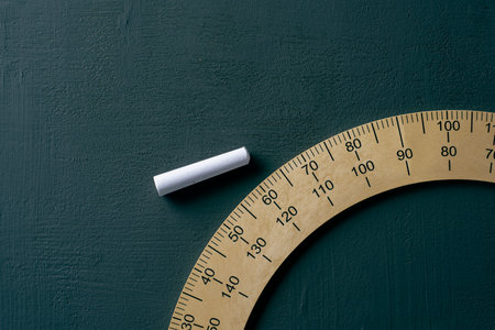 closeup of a protractor and a piece of chalk on a dark green chalkboard