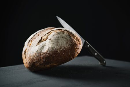 a pan de payes, a round bread typical of Catalonia, Spain, and a knife on a dark green surfaceの写真素材