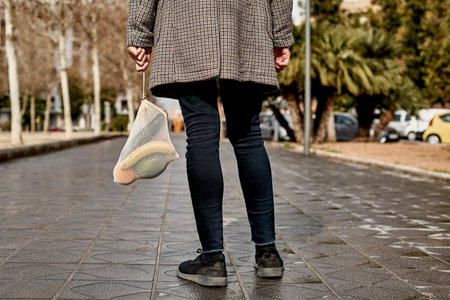 closeup of a man in the street, seen from behind, carrying a textile reusable mesh bag, used to buy...