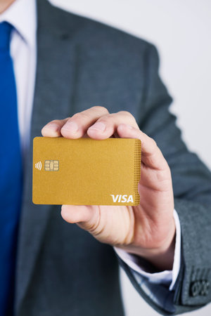 BARCELONA, SPAIN - FEBRUARY 13, 2020: A businessman, in an elegant gray suit, shows a Visa Gold credit cardのeditorial素材