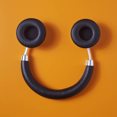 high angle view of a pair of black wireless full size headphones upside down on an orange background, resembling a smiley faceの写真素材